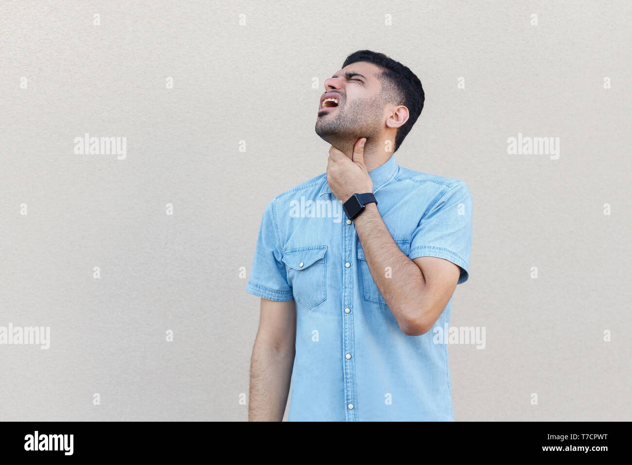 Maux de gorge, de maladie ou de froid grippe. Portrait d'un beau jeune homme barbu en chemise bleue debout et tenant son cou. Piscine studio shot isoler Banque D'Images