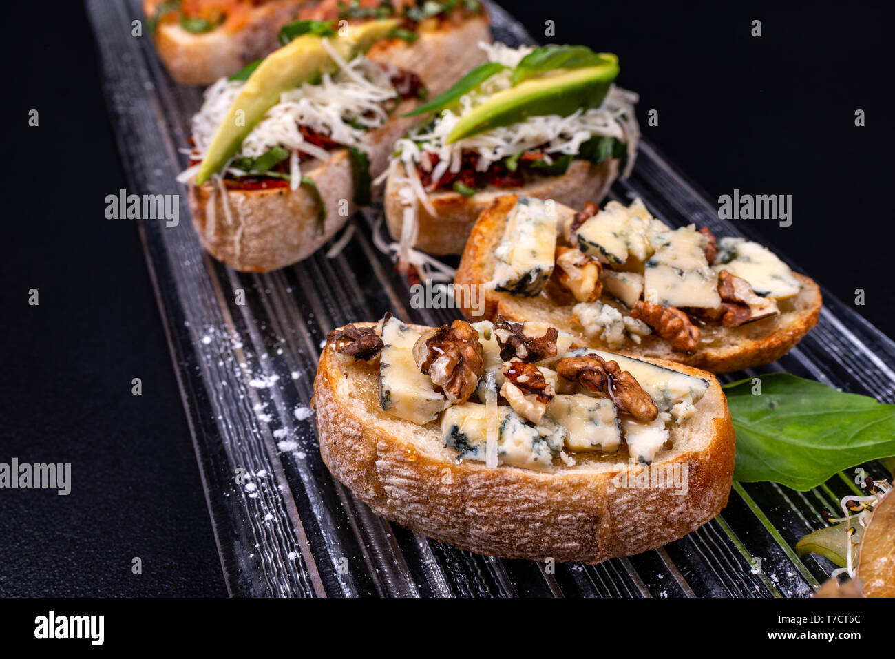 Bruschetta apéritif avec du fromage, miel, noix et d'autres ingrédients sur fond noir. Close-up. Cuisine italienne. Banque D'Images