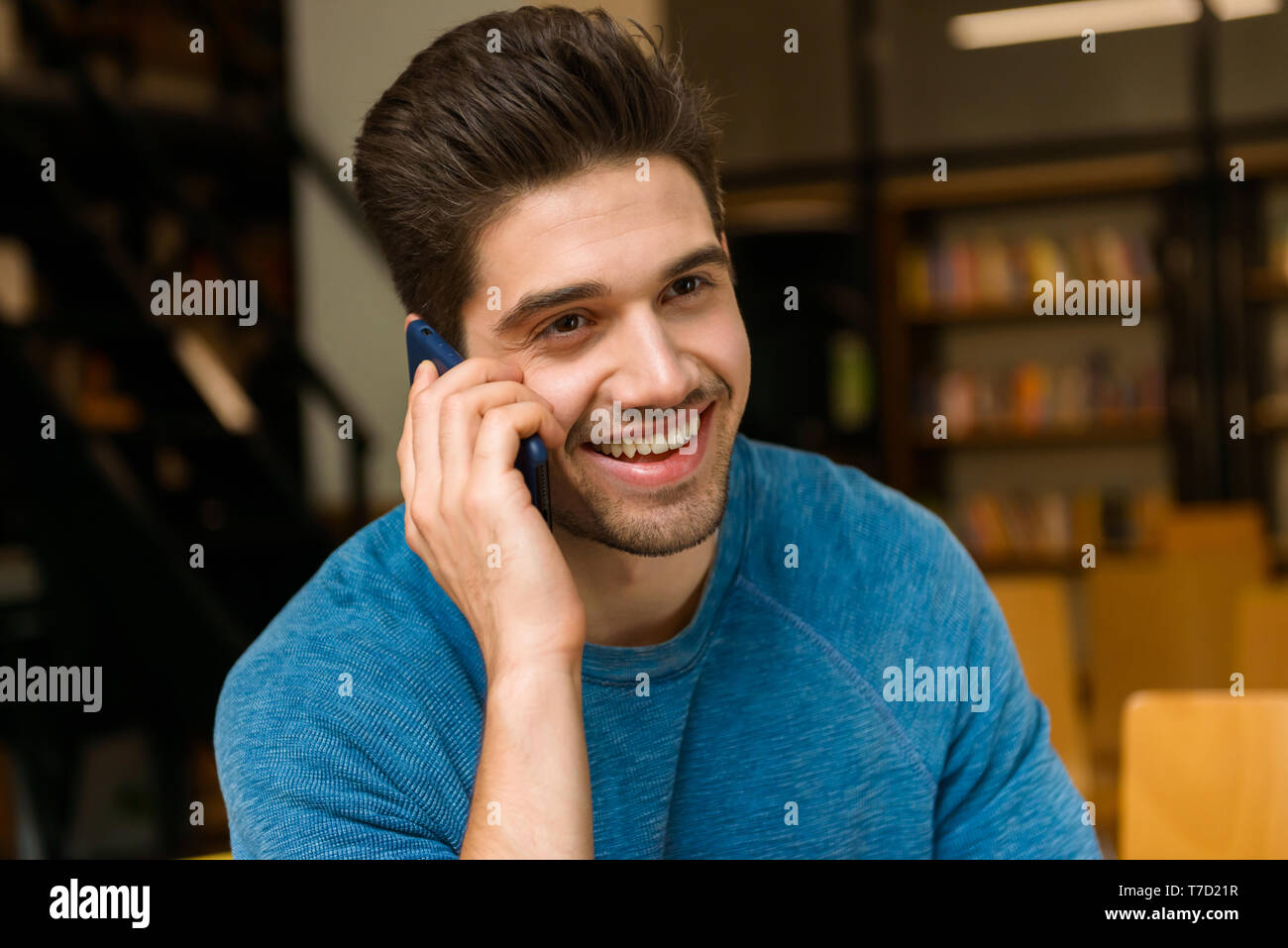 Image d'un jeune homme étudiant dans la bibliothèque à faire des devoirs l'étude de parler par téléphone mobile. Banque D'Images