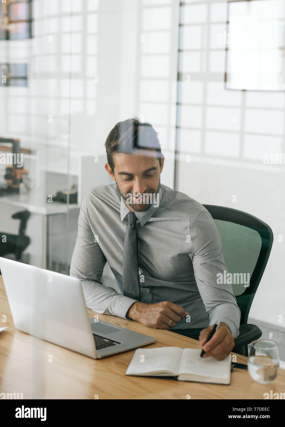 Smiling businessman sitting au travail de rédaction idées dans un ordinateur portable Banque D'Images