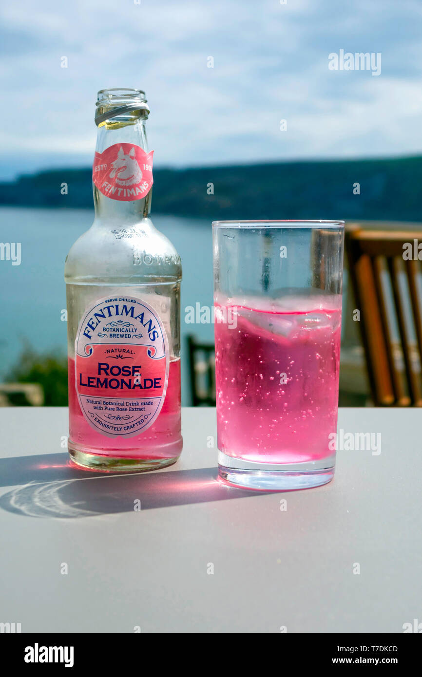 Un verre et une bouteille de mousseux Fentimans froid Limonade rose sur une table d'extérieur par la mer Banque D'Images