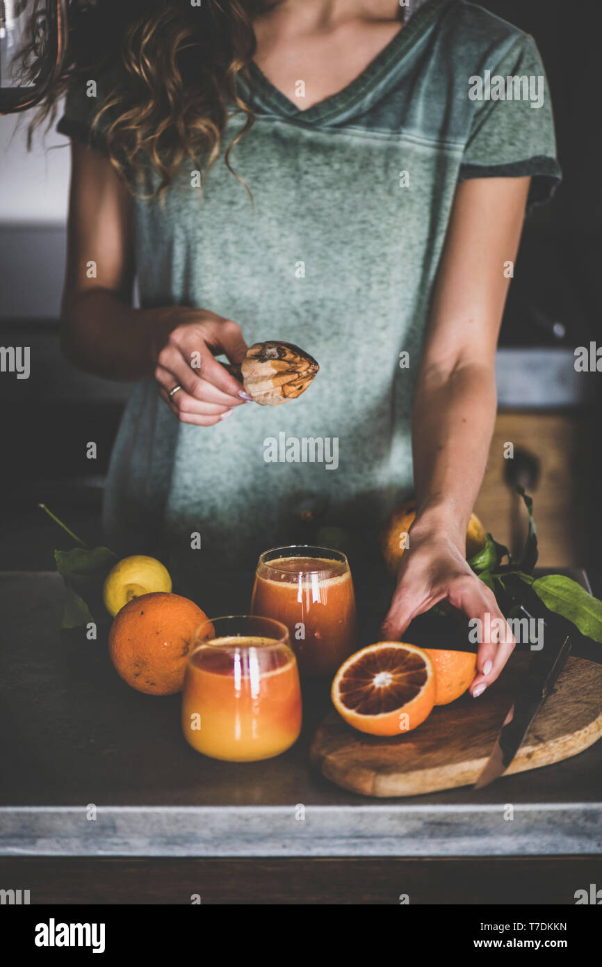 Jeune femme faisant du sang fraîchement pressé ou de jus d'orange smoothie près de comptoir de cuisine en béton. Mode de vie sain, végétarien, végétalien, régime alcalin Banque D'Images