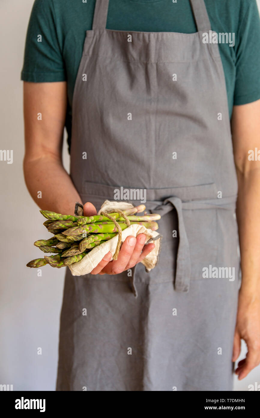 L'homme en tablier gris fond blanc avant la tenue d'un ensemble d'asperges vertes dans une serviette dans ses mains Banque D'Images