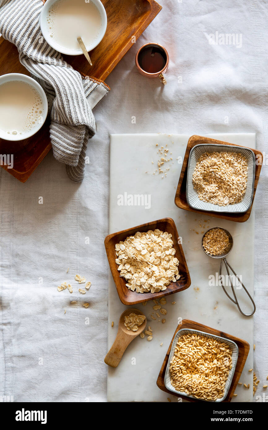 Grains d'avoine, flocons d'avoine, l'avoine et le lait d'avoine dans l'eau au moulin des bols en bois blanc et de tasses sur le marbre blanc sur fond blanc Banque D'Images