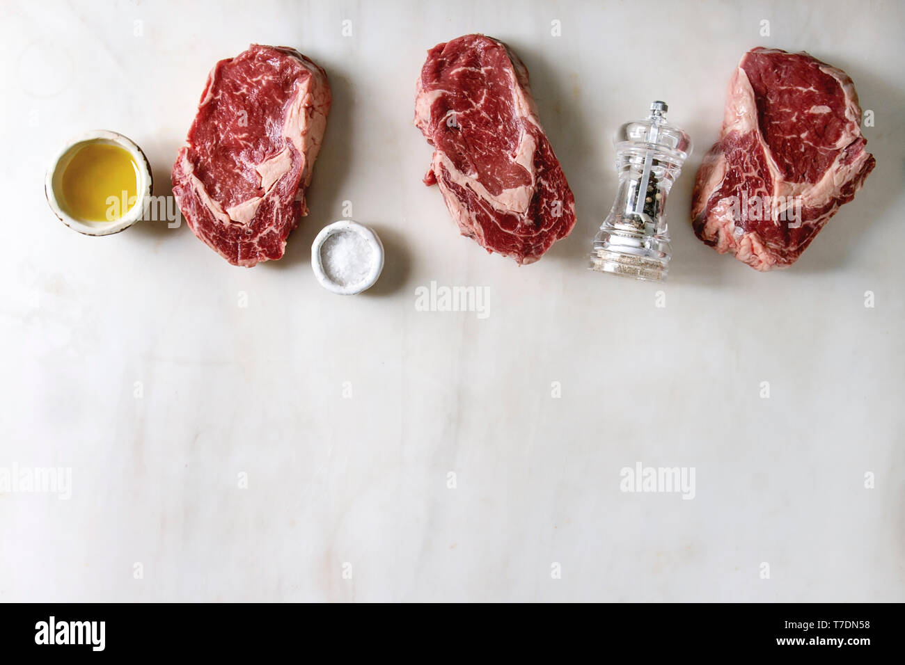 Trois matières du boeuf cru steaks avec poivre, sel et huile d'olive dans la rangée sur fond de marbre blanc. Mise à plat, de l'espace Banque D'Images