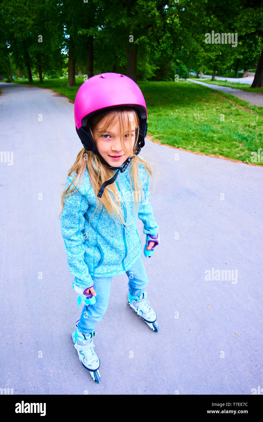 Jolie petite fille enfant apprendre à roller skate sur belle journée d'été dans un parc. Enfant portant un casque de sécurité jouissant de roller ride outdoors Banque D'Images