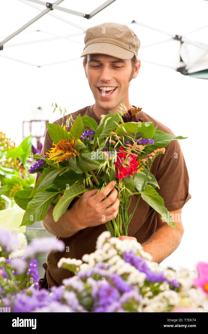 Smiling man vendeur vente de fleurs fraîches au marché de fermiers, Whidbey Island, WA, United States. Des gens locaux sympathiques dans le nord-ouest du Pacifique. Banque D'Images