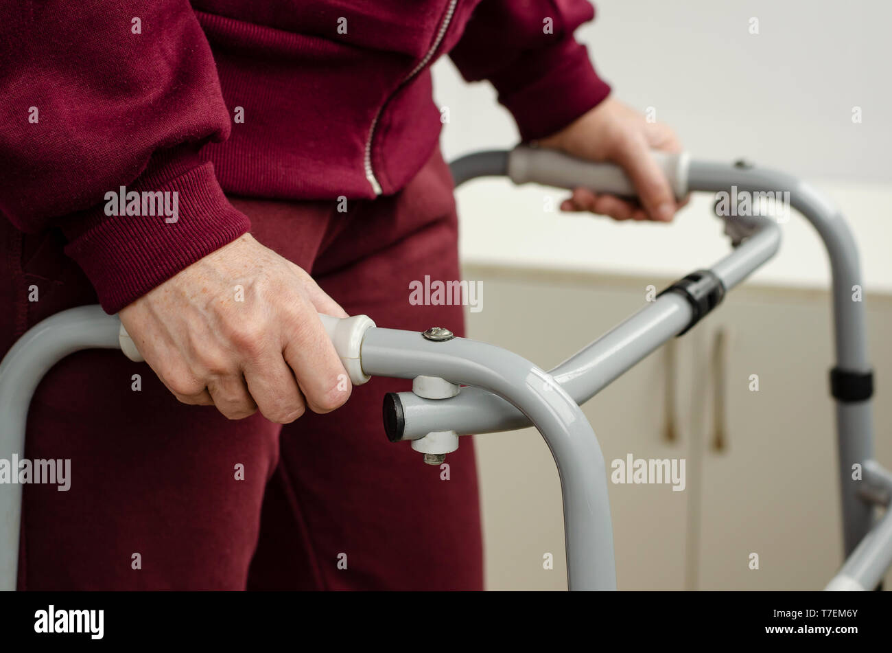 Hauts femme debout et marcher avec ses mains sur les poignées d'une marchette. Les soins de réadaptation et de concept. Banque D'Images