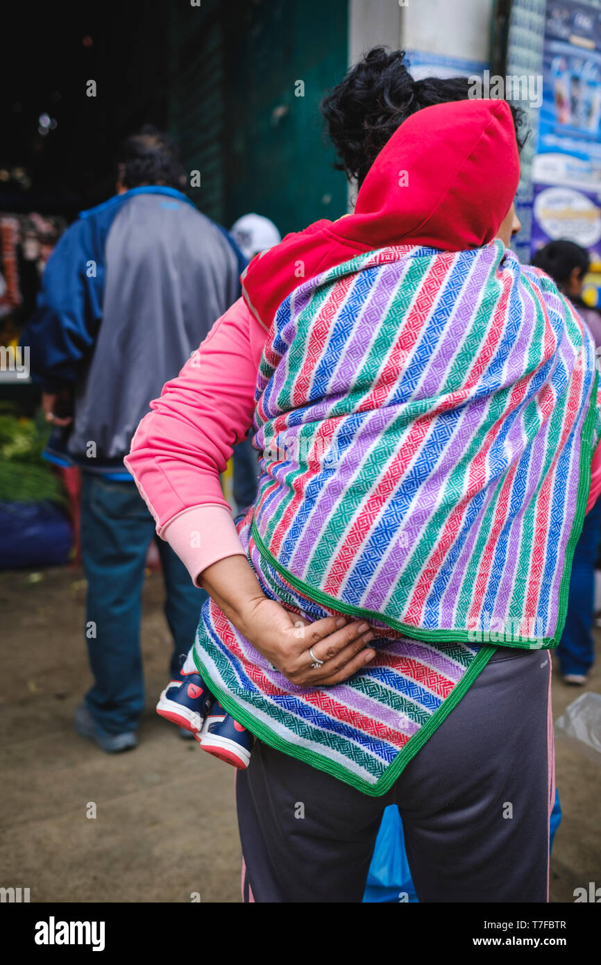Femme portant son bébé sur un classique sac style Péruvien colorés dans les rues de Barranca, région de Lima, Pérou Banque D'Images