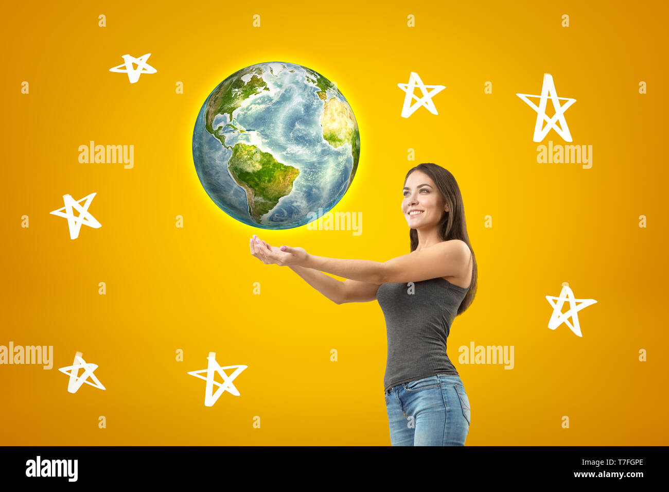 Young smiling brunette girl wearing jean décontracté et t-shirt avec les paumes vers le haut, earth globe et personnages tirés sur fond jaune Banque D'Images