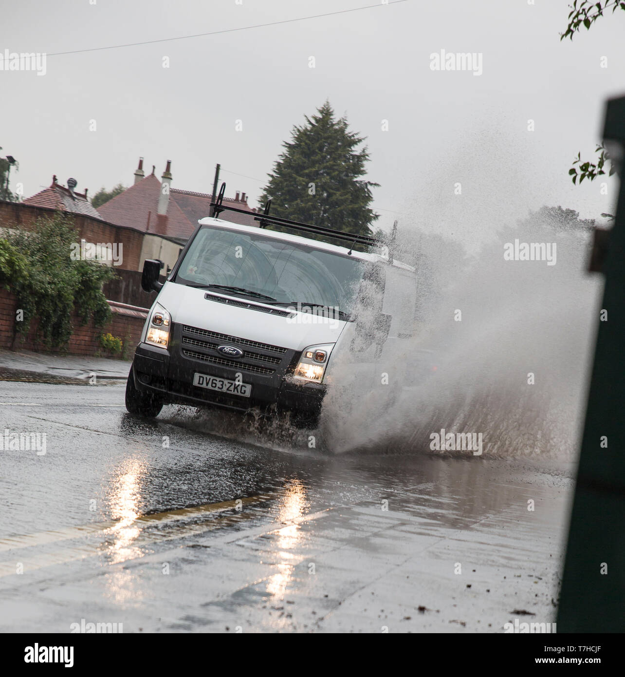 Vue avant du van blanc isolé, les phares, le comité permanent de l'eau éclaboussant par inondation sur UK road. UK flash inondations dues à des problèmes de vidange bouché. Banque D'Images