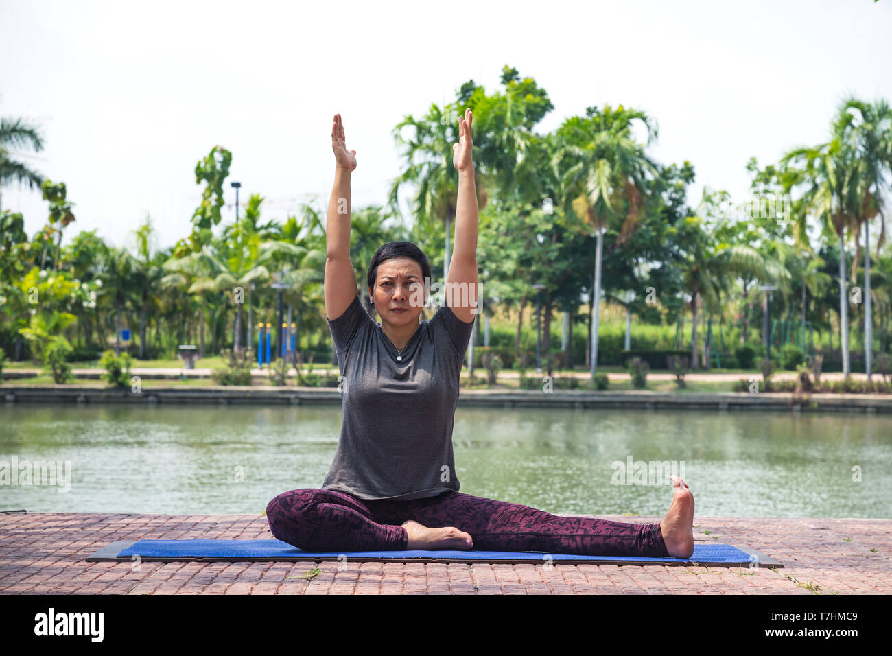 Femme asiatique sains d'âge moyen assis et lever les bras pour commencer le yoga de poser dans les parc de la ville au matin et le mode de vie sain. concept. Banque D'Images