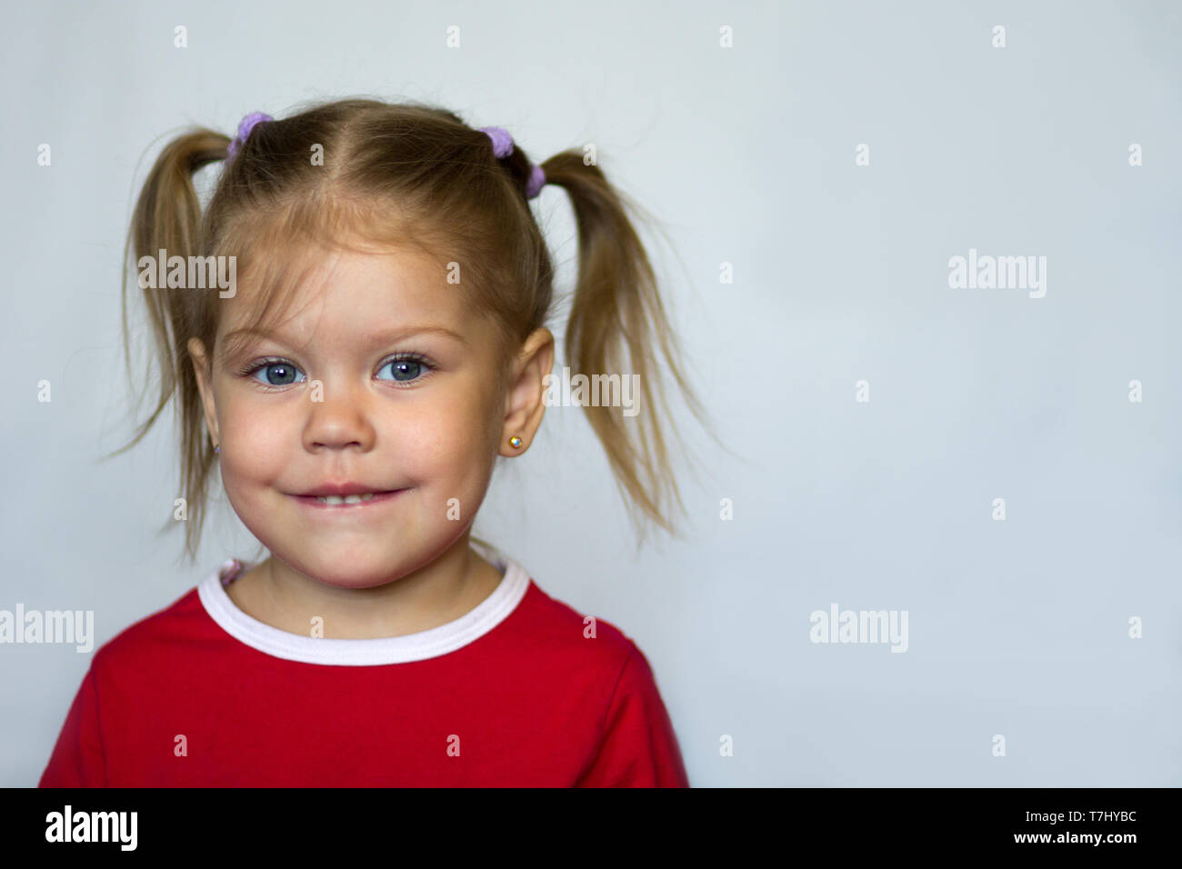 Portrait de petite fille aux yeux bleus de mordre la lèvre inférieure à la caméra à sur le fond blanc Banque D'Images