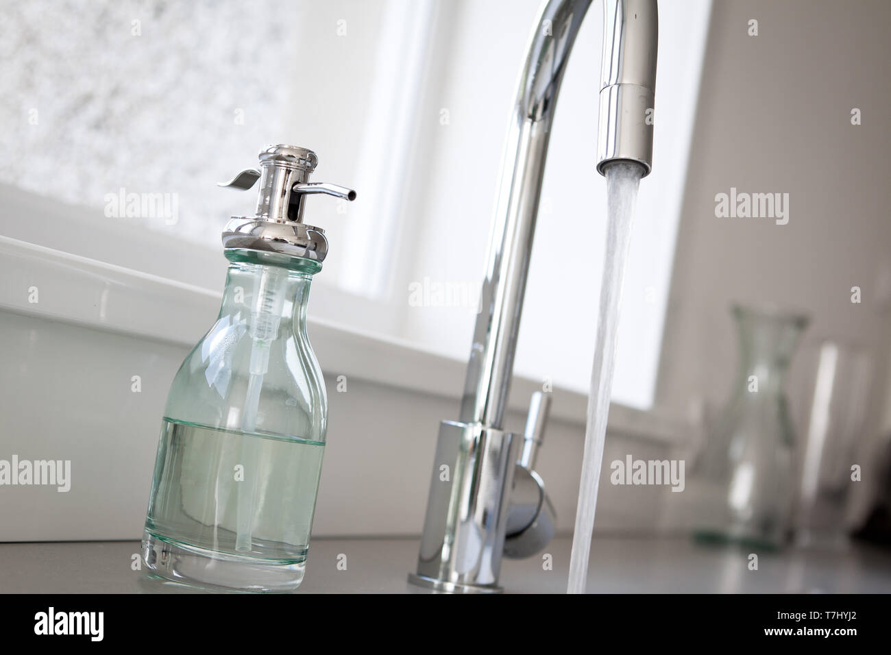Un robinet ouvert à la maison d'un évier. Également sur la photo est une bouteille de lavage à la main. Banque D'Images