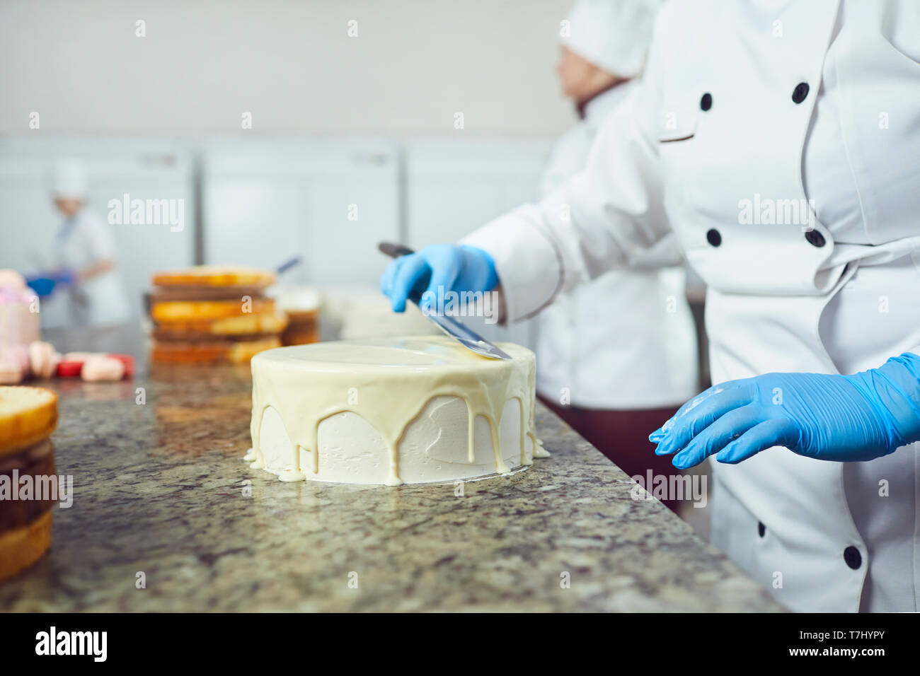 Mains crème confiseur s'étend sur un gâteau blanc sur la table dans la pâtisserie Banque D'Images