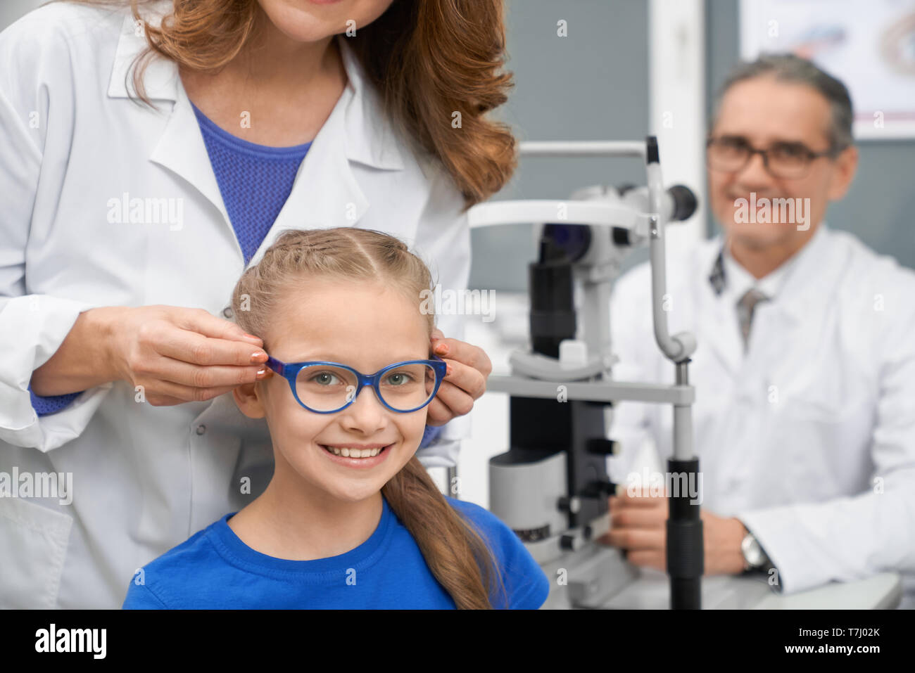 Test de la vue patient médecin optométriste. Travailleur de la santé en manteau blanc choisir lunettes pour adolescent. Fille en bleu verres assis, souriant et regardant la caméra. Cabinet d'ophtalmologie. Banque D'Images