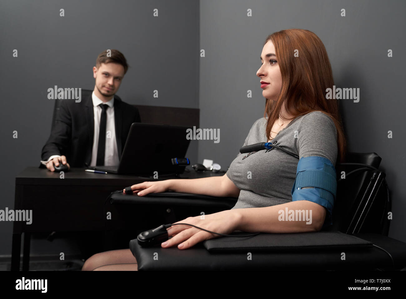 Femme assise dans un fauteuil avec les capteurs de doigt joint et le fil et l'essai avec détecteur de mensonge. Jeune homme à table avec ordinateur polygraphe, mensonge ou vérité suivi. Banque D'Images