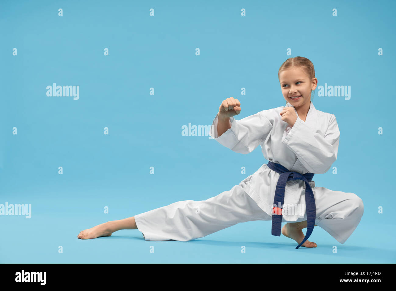 Happy little girl wearing kimono de karaté permanent position et exercer en studio. Femme forte à côté sur adversaire chid et faisant fond sur des arts martiaux. Concept de sport. Banque D'Images