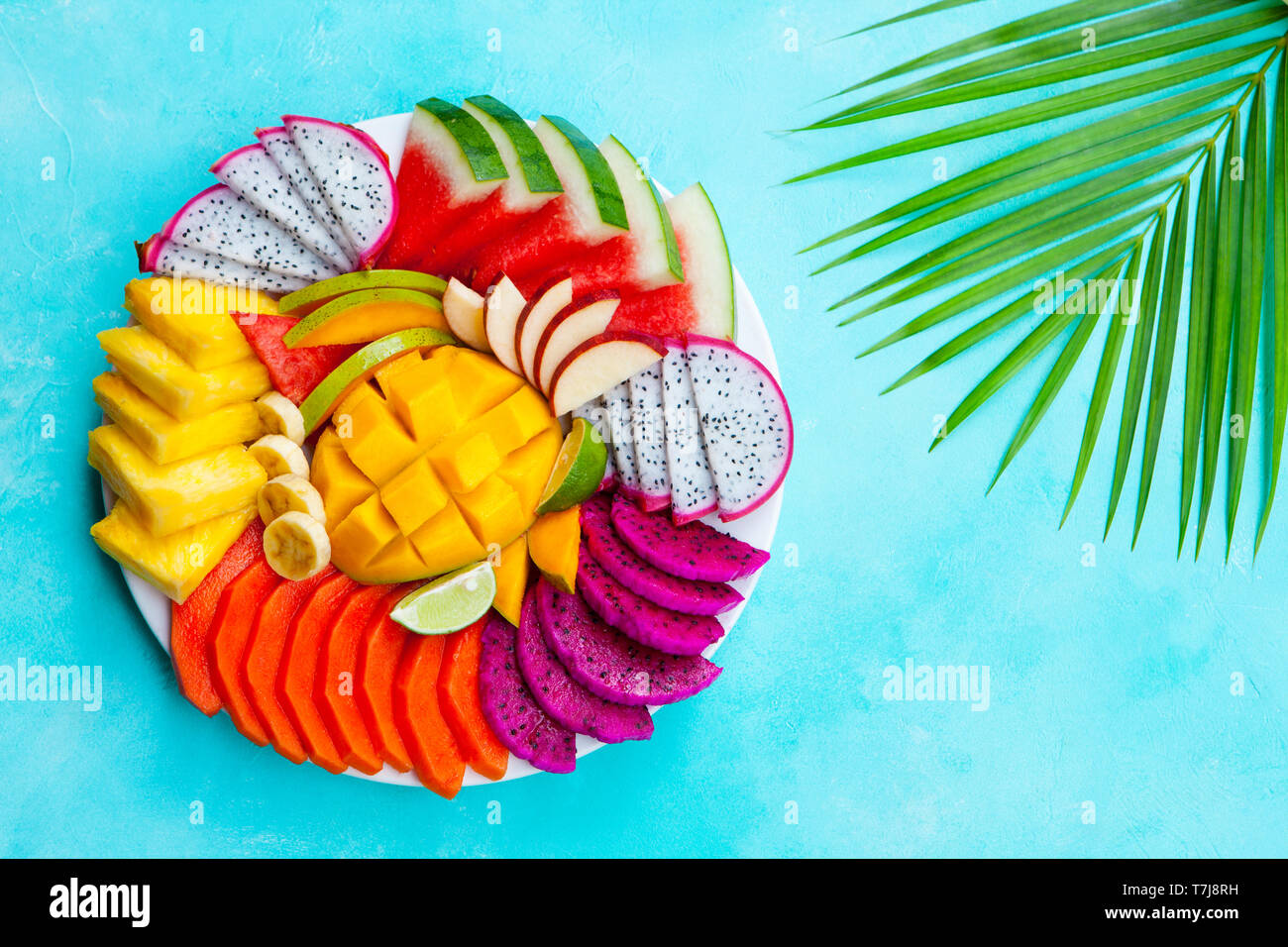Assortiment de fruits tropicaux sur une plaque blanche avec feuille de palmier. Fond bleu. Vue d'en haut. Copier l'espace. Banque D'Images