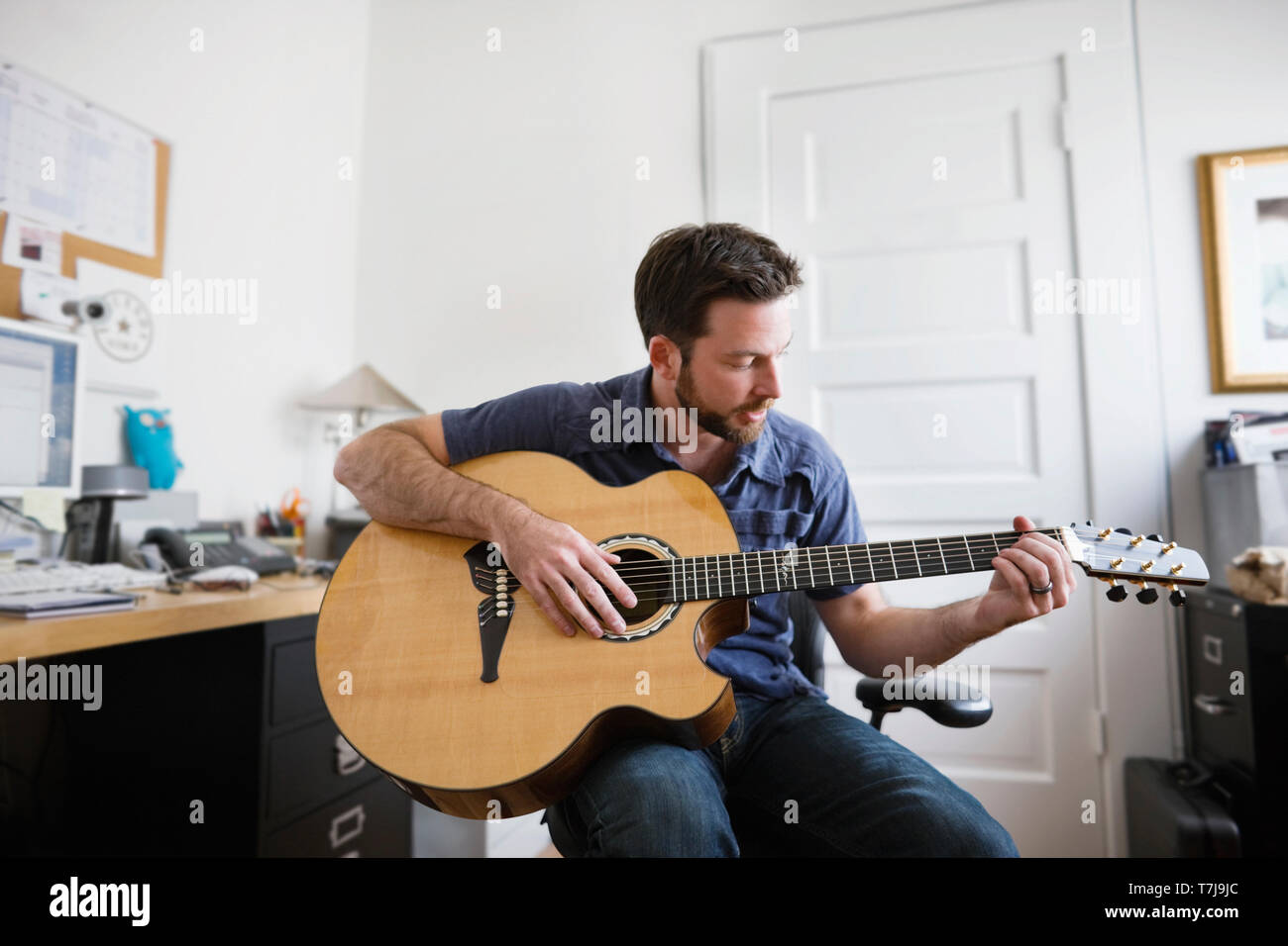 Jeune adulte homme jouant une guitare acoustique dans un bureau à domicile. Banque D'Images