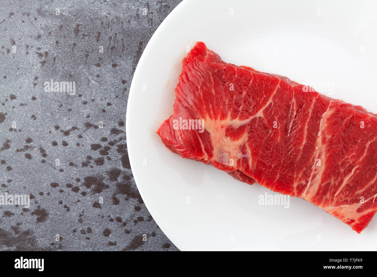 Haut de page Fermer la vue d'une seule pièce de boeuf désossé côtes courtes chuck steak de cuisson sur une plaque blanche sur un comptoir gris éclairés par la lumière naturelle Banque D'Images
