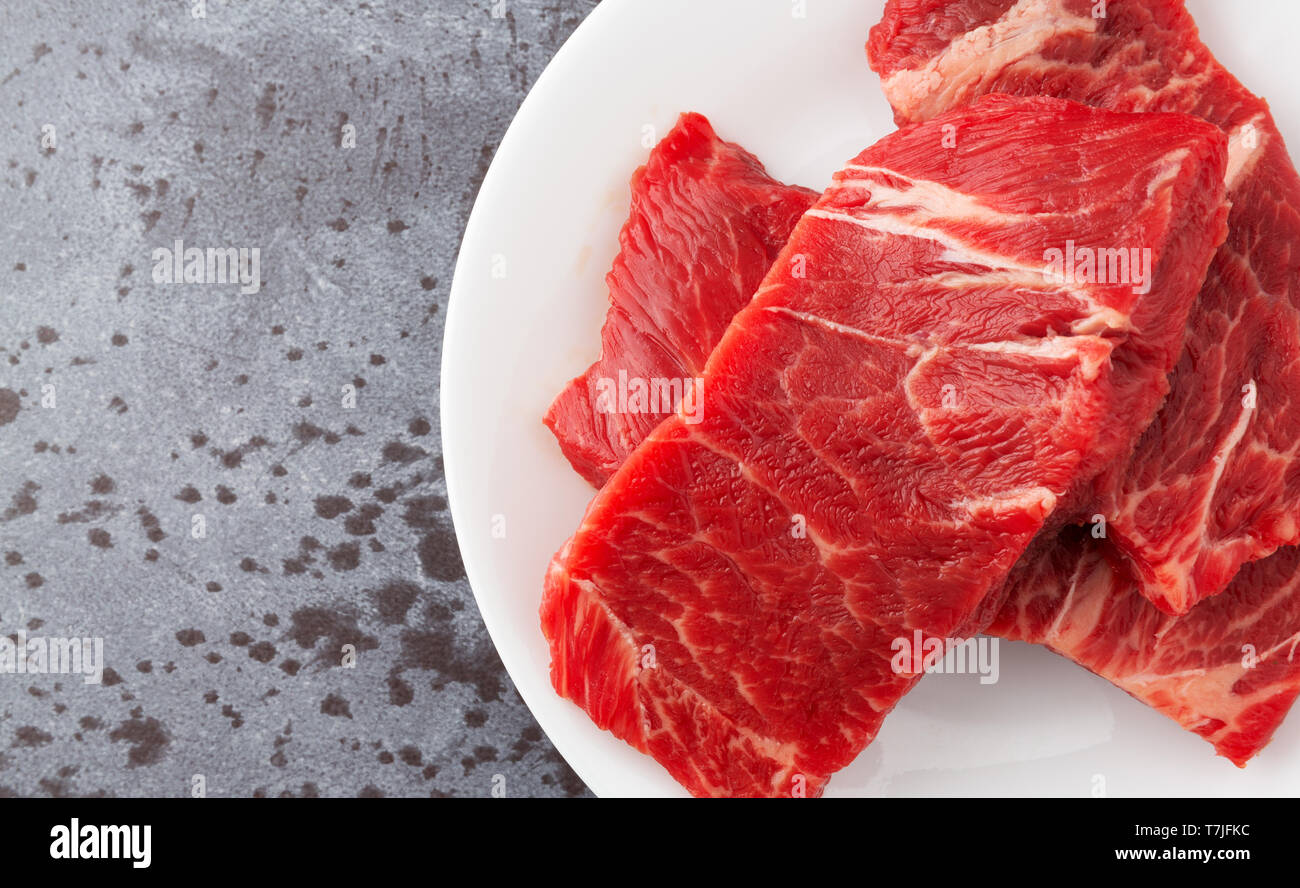 Haut de page Fermer la vue de plusieurs pièces de viande bovine désossée côtes chuck courte cuisson steaks sur une plaque blanche sur un comptoir gris naturel éclairé avec ligh Banque D'Images