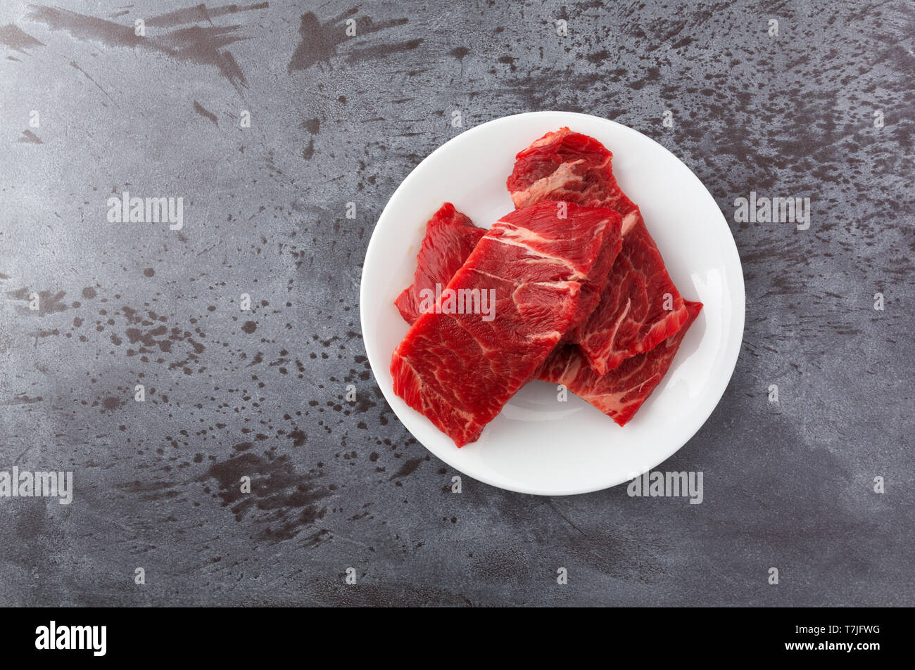 Vue de dessus de plusieurs morceaux de viande bovine désossée côtes chuck courte cuisson steaks sur une plaque blanche sur un comptoir gris éclairés par la lumière naturelle. Banque D'Images