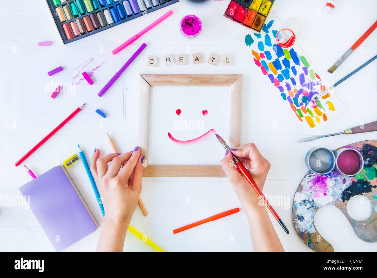 Vue de dessus les mains de sexe féminin sourire dessin sur toile avec word créer un lettrage et de nombreux matériaux paintiing colorés sur fond blanc. Ajouter des couleurs à votre Banque D'Images