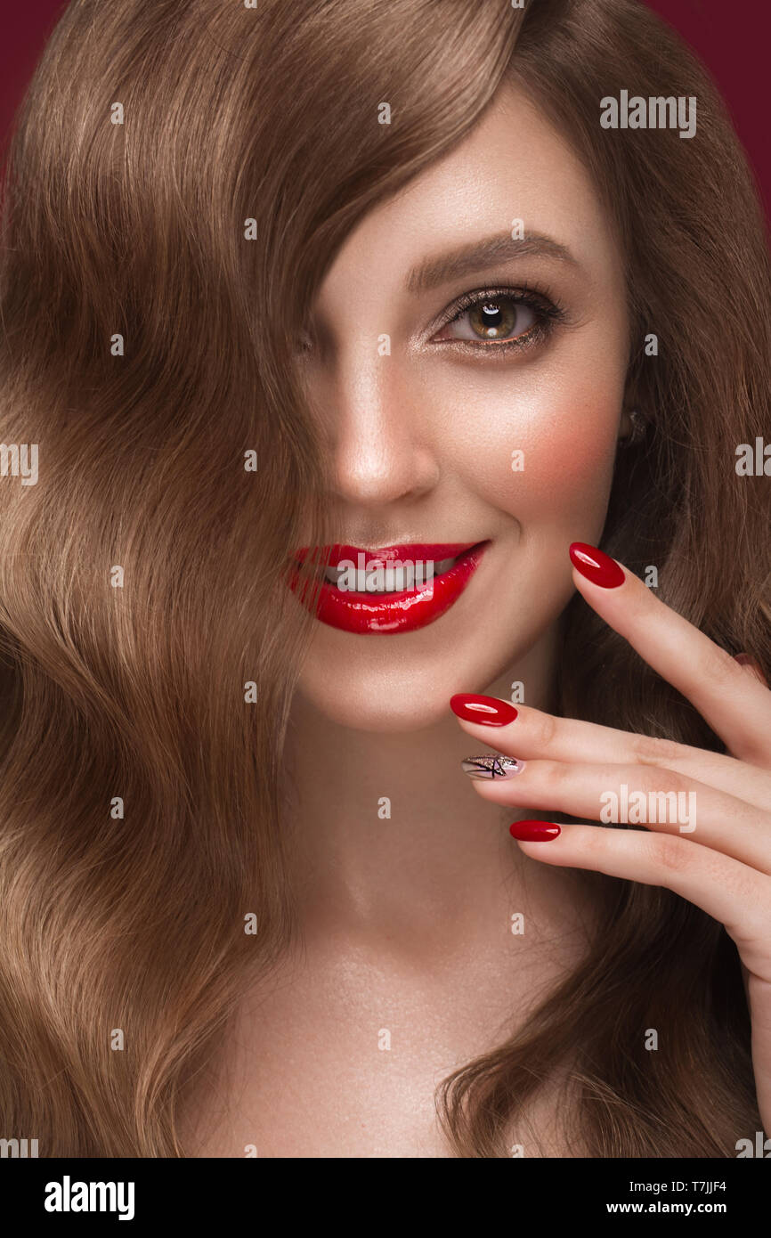 Belle fille avec un maquillage classique, les boucles des cheveux et des ongles rouges. Conception de manucure. Beauté Visage. Banque D'Images