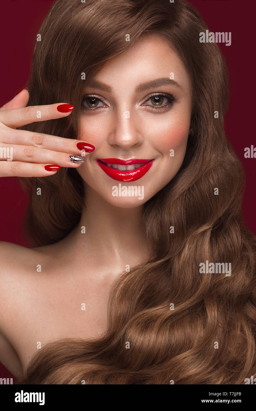 Belle fille avec un maquillage classique, les boucles des cheveux et des ongles rouges. Conception de manucure. Beauté Visage. Banque D'Images