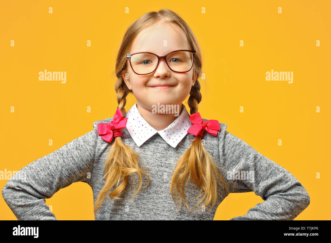 Portrait of a cute little baby girl avec des lunettes sur un fond jaune. La lycéenne fait mains dans ses hanches et se penche sur l'appareil photo. Le concep Banque D'Images
