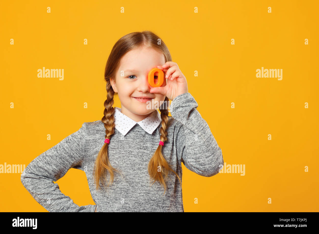 Portrait d'un joyeux petit enfant fille sur un fond jaune. Lycéenne tient la lettre O. Le concept de l'éducation. Banque D'Images