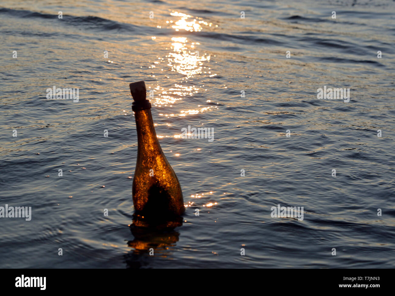 Le flacon en verre contenant un message flottant dans les vagues de la mer au coucher du soleil Banque D'Images