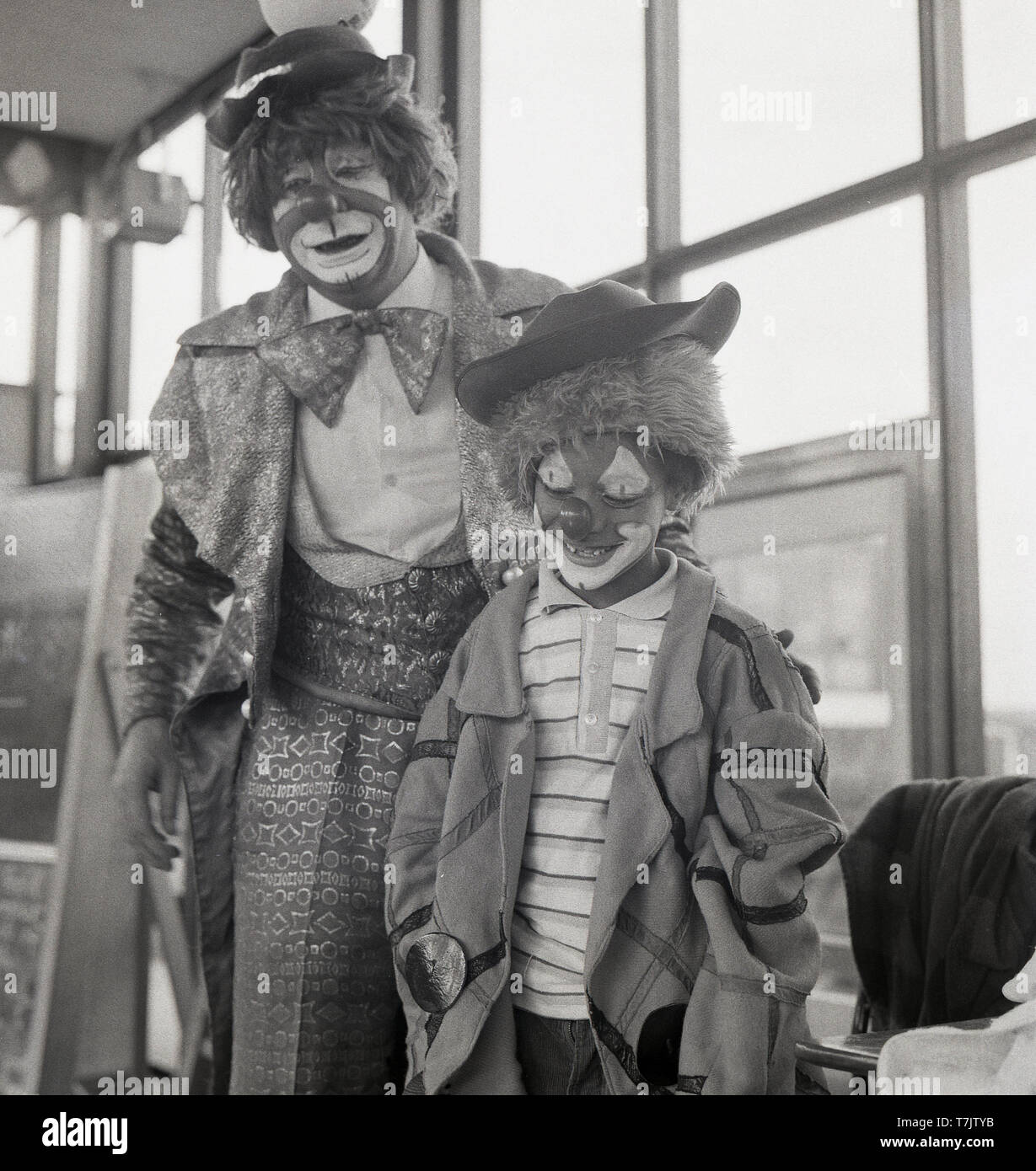 Années 1960, historique, un clown de cirque visiter une école primaire avec un jeune écolier portant robe et avec son visage peint comme un clown, England, UK. Banque D'Images