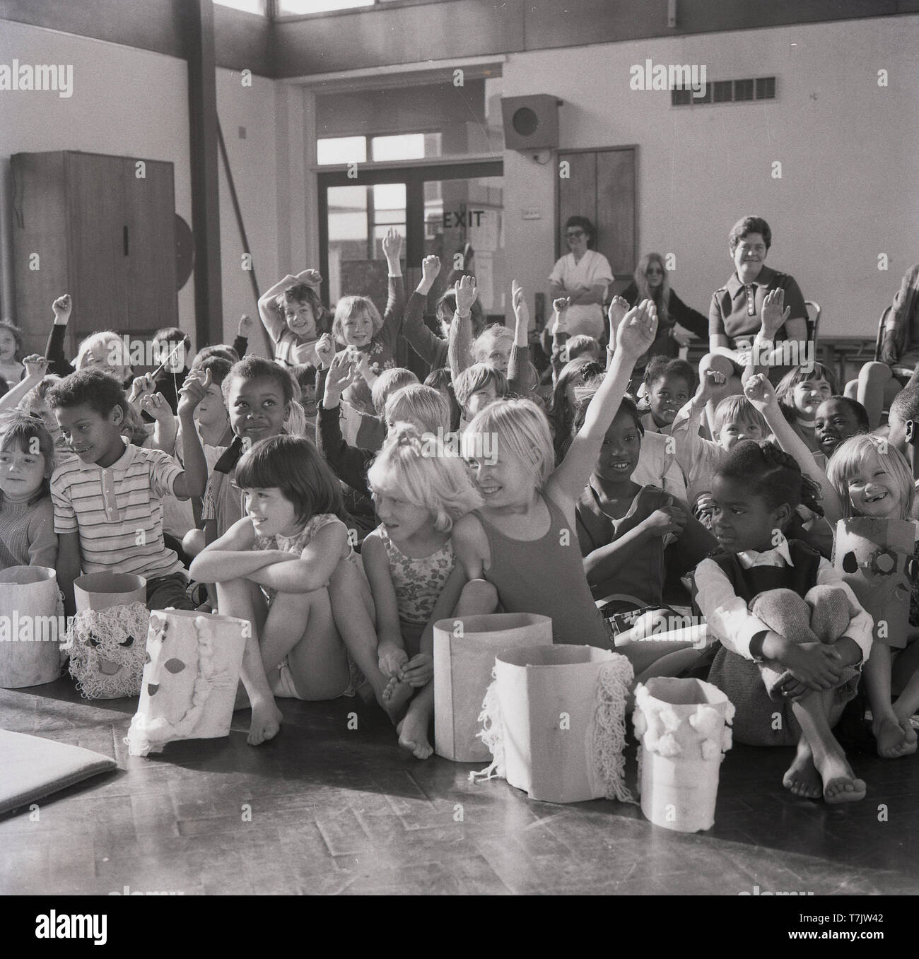 Années 1960, historiques, excité les jeunes enfants de l'école dans la salle d'école leur main pour poser une question, England, UK. Banque D'Images