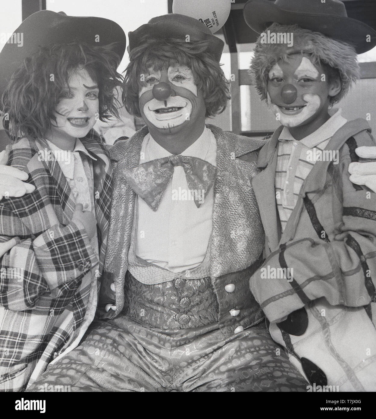 Années 1960, historique, un clown de cirque avec deux jeunes enfants de l'école habillés et avec leurs visages peints comme un clown, England, UK. Banque D'Images