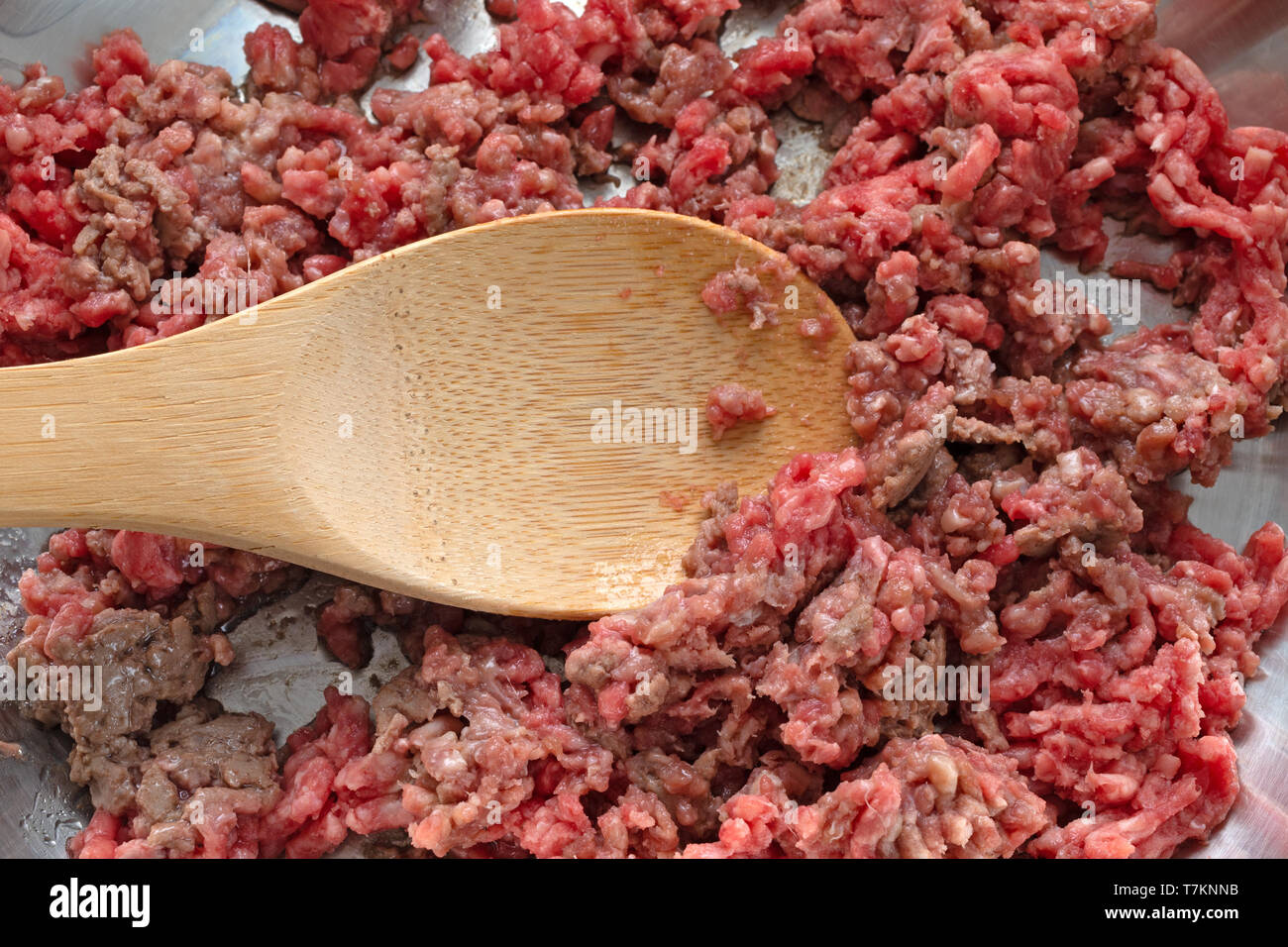 Gros plan de cuisson du boeuf haché dans une poêle avec une cuillère en bois éclairé par la lumière naturelle. Banque D'Images