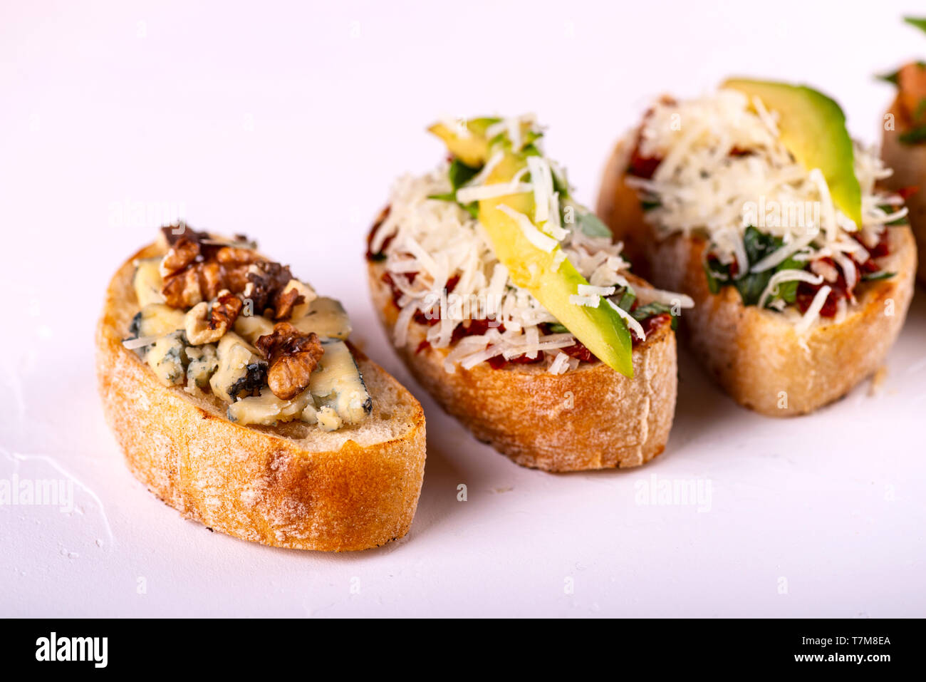 Brushetta défini pour un apéritif. Variété de petits sandwiches avec tomates, fromage parmesan, avocat et noix servi sur un fond blanc Banque D'Images