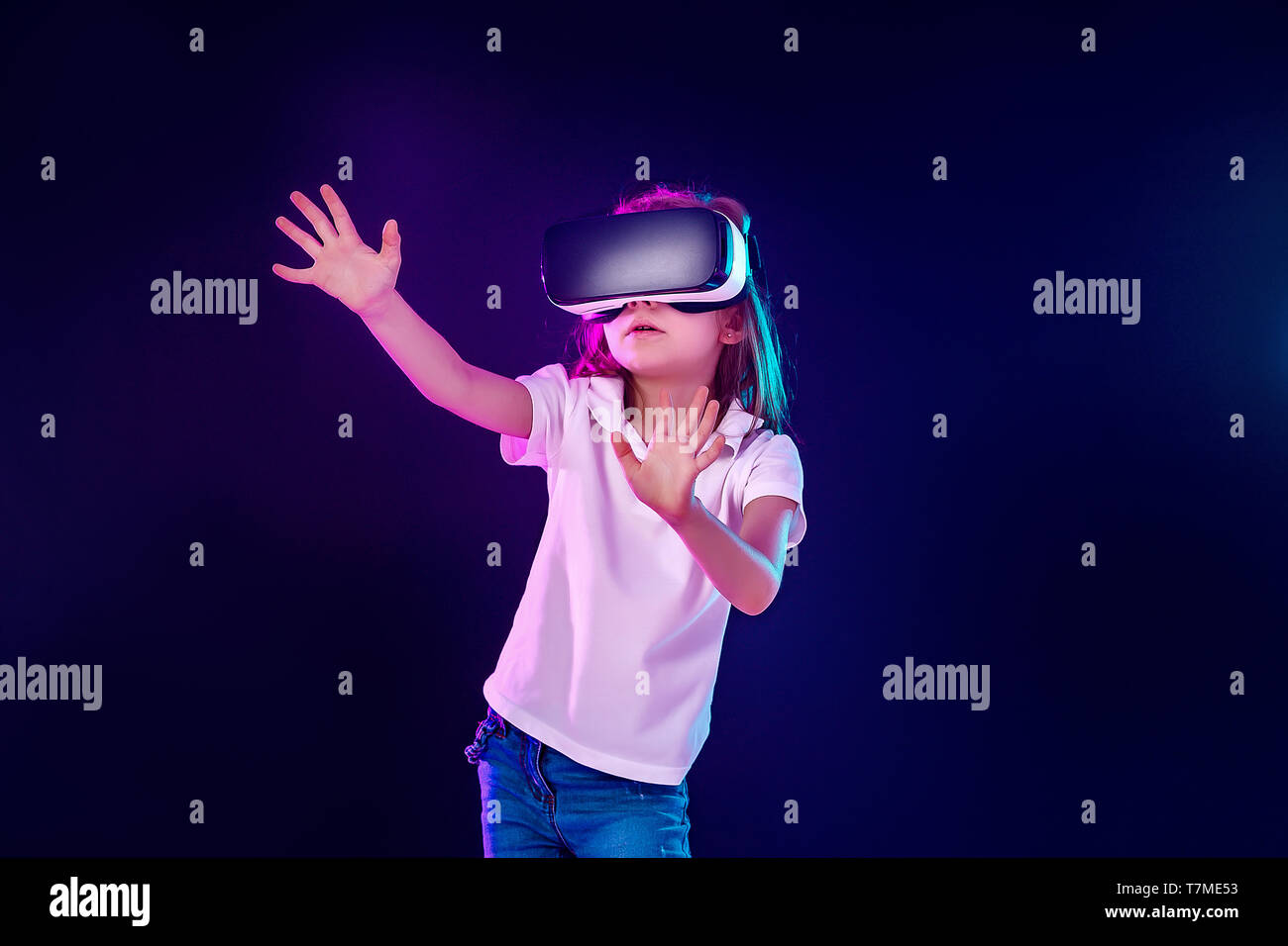 Fille 7 ans expérience de jeu casque VR sur fond coloré. Enfant à l'aide  d'un gadget de jeu de réalité virtuelle. Lunettes futuriste à un jeune âge.  La technologie virtuelle Photo Stock -