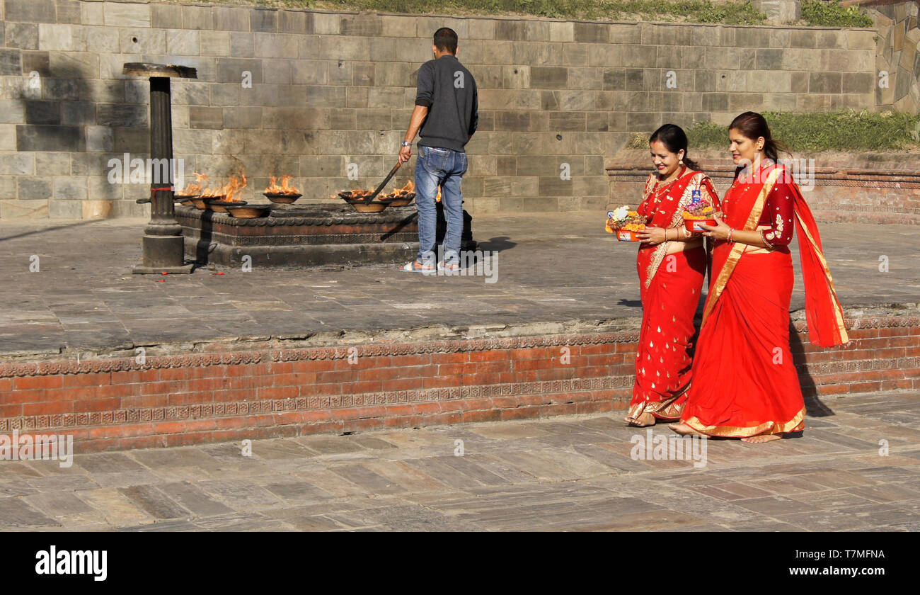 Les femmes en saris colorés rouge et or faire offrandes religieuses passé lieu de rituel du feu, temple hindou de Pashupatinath, Vallée de Katmandou, Népal Banque D'Images