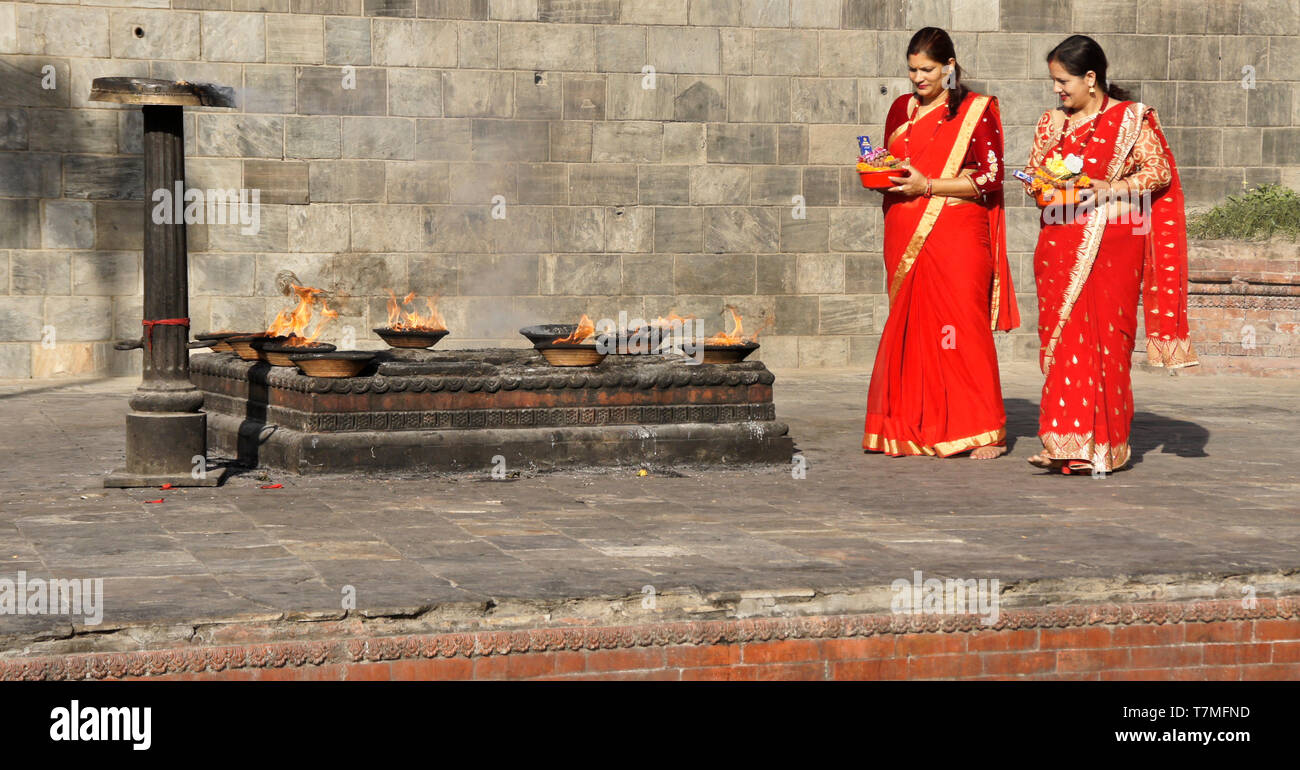 Les femmes en saris colorés rouge et or avec des offrandes religieuses au lieu de rituel du feu, temple hindou de Pashupatinath, Vallée de Katmandou, Népal Banque D'Images