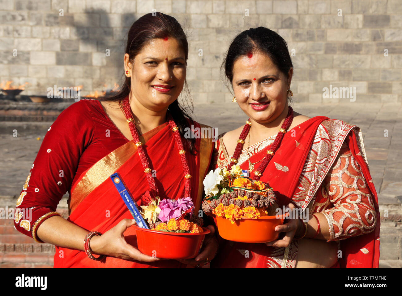 Les femmes en saris colorés rouge et or avec des offrandes religieuses au lieu de rituel du feu, temple hindou de Pashupatinath, Vallée de Katmandou, Népal Banque D'Images