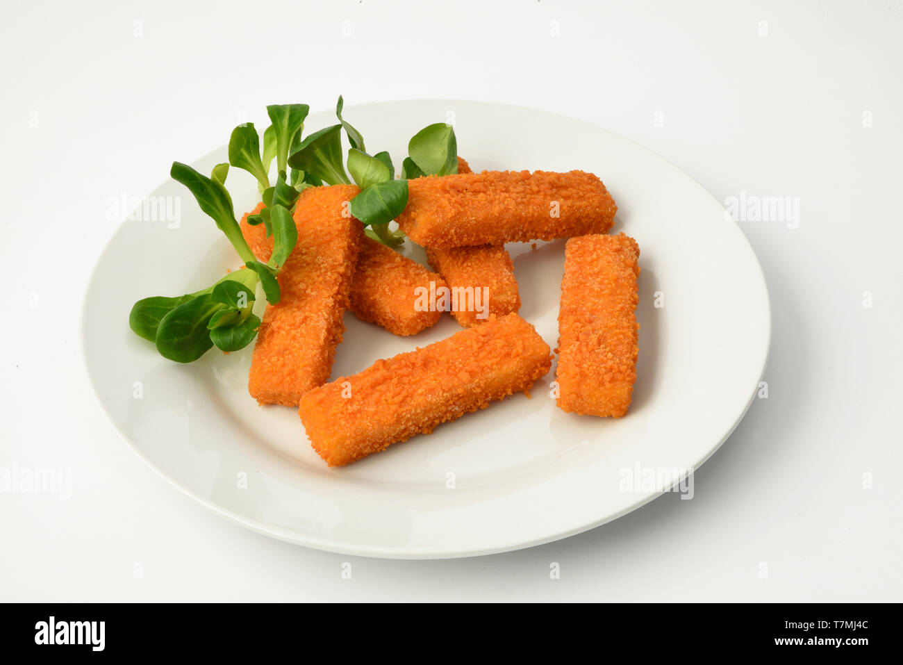 Les bâtonnets de poisson, les bâtonnets de poisson sur une assiette blanche, décorée avec une salade de maïs. Studio photo sur un fond blanc. Banque D'Images