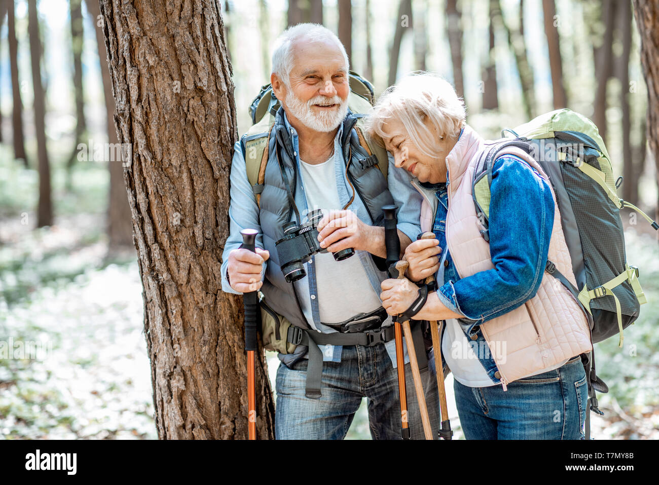 Senior couple reposant près de l'arbre lors d'un voyage avec les sacs à dos et bâtons de trekking dans la forêt. Concept d'une vie active à la retraite Banque D'Images