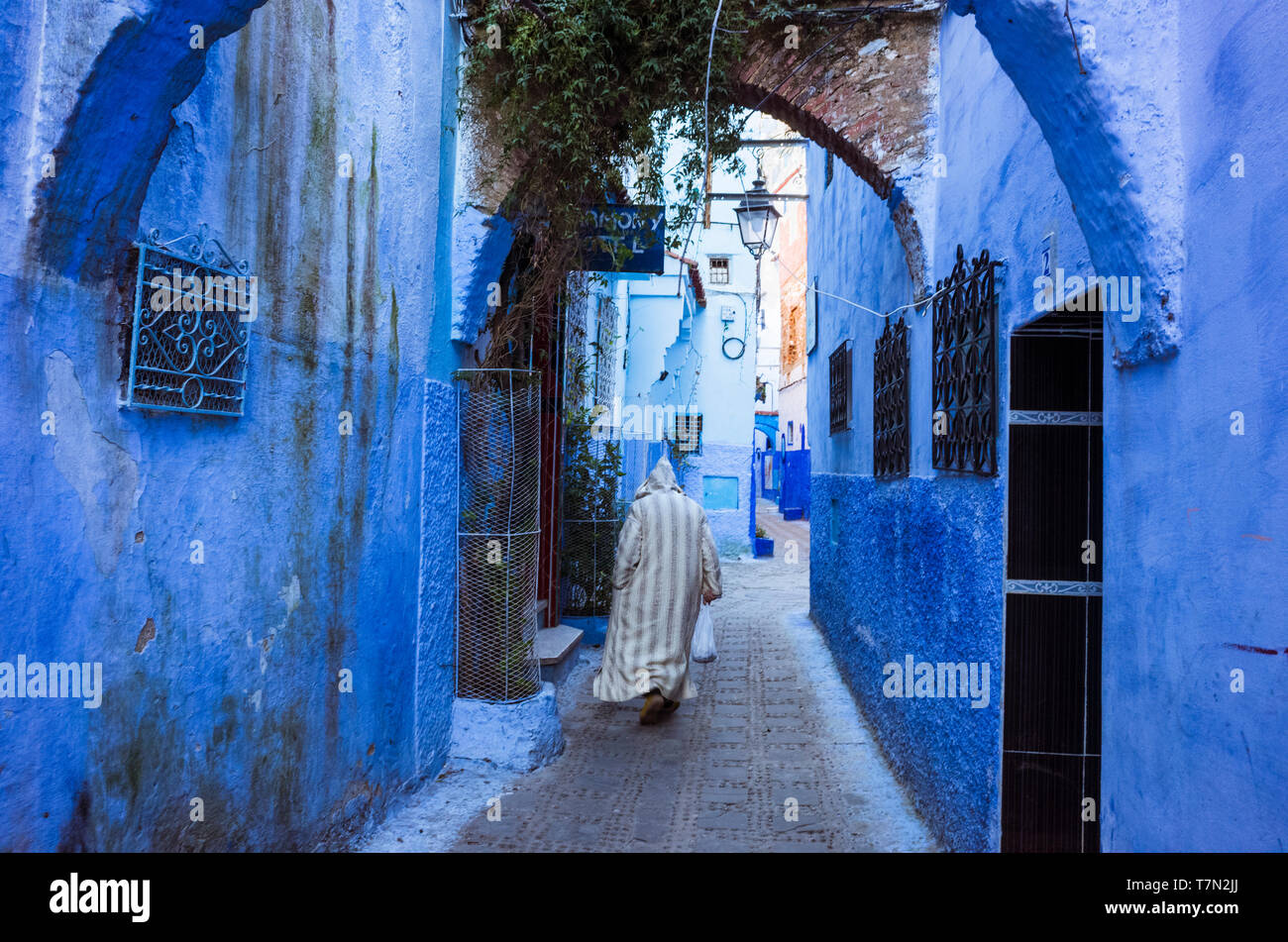 Chefchaouen, Maroc : un homme portant une djellaba traditionnelle promenades dans le bleu à la chaux ruelles de la médina, vieille ville. Banque D'Images