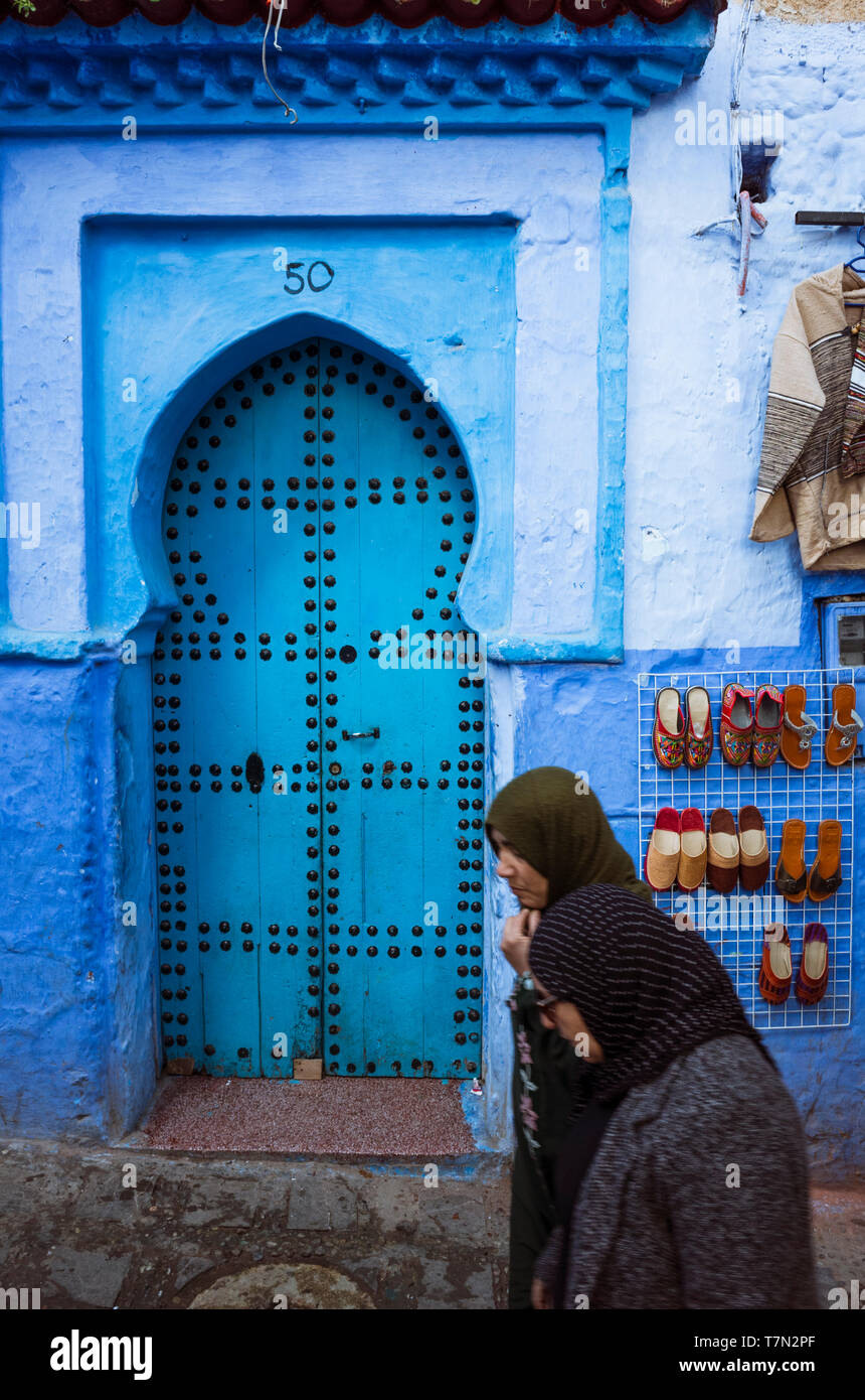 Chefchaouen, Maroc : Deux femmes devant une porte en bois traditionnel dans le bleu à la chaux medina vieille ville. Banque D'Images