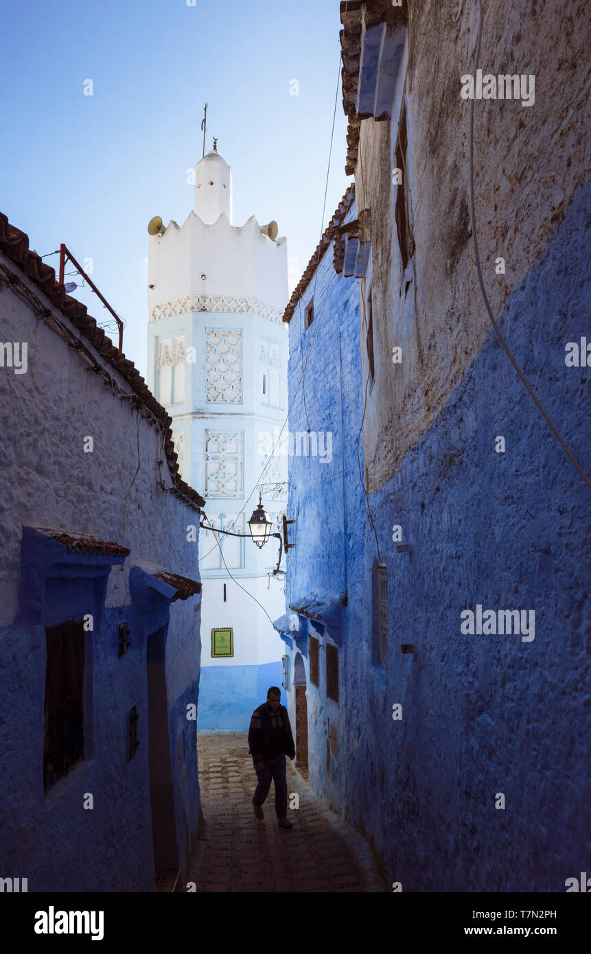 Chefchaouen, Maroc : un homme marche dans une ruelle lavés sous le minaret d'une mosquée dans la médina. Banque D'Images