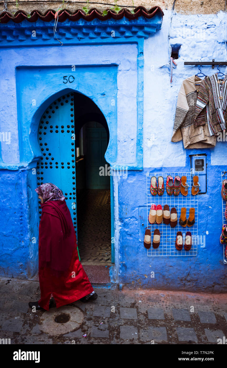 Chefchaouen, Maroc : une femme passe devant une porte en bois traditionnel dans le bleu à la chaux medina vieille ville. Banque D'Images