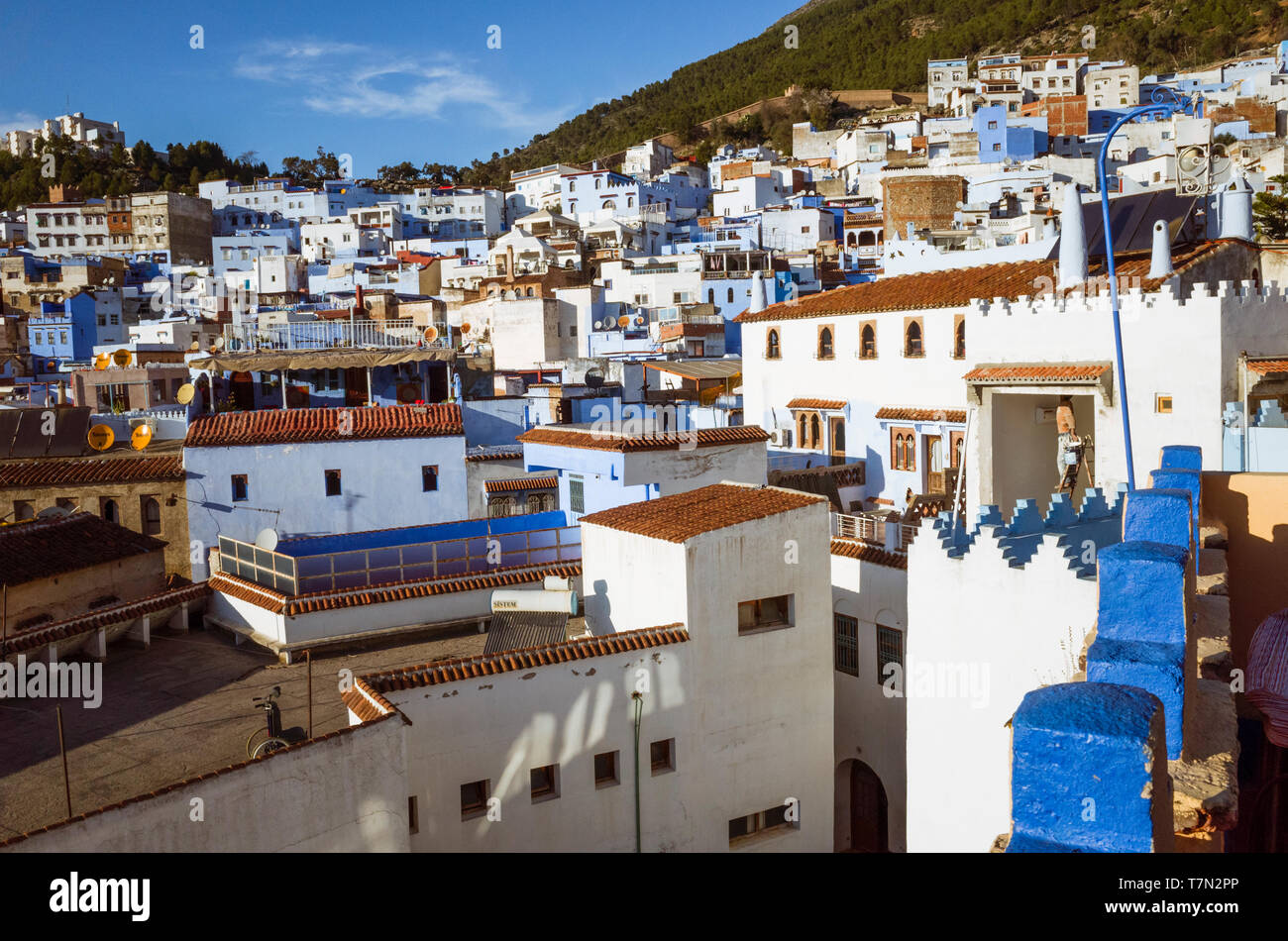 Chefchaouen, Maroc : Un homme peint une maison entourée par les toits de la médina, vieille ville, bien connu pour son architecture bleu-lavés. Banque D'Images