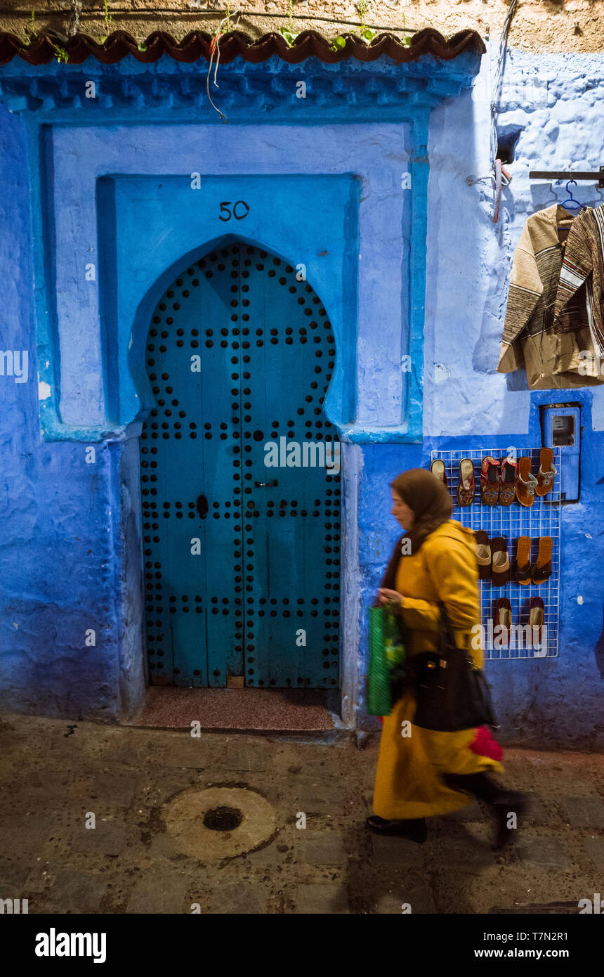 Chefchaouen, Maroc : une femme passe devant une porte en bois traditionnel dans le bleu à la chaux medina vieille ville de nuit. Banque D'Images